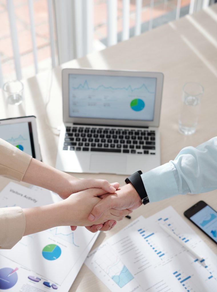 Hands of business people shaking hands over table with various charts and reports after having successful meeting